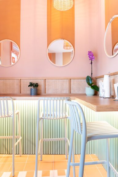 Interni di un ristorante, con pareti rosa, specchi rotondi e piante verdi.